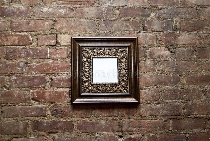 An empty ornamental frame hanging on a brick wall. An empty ornamental frame hanging on a brick wall.