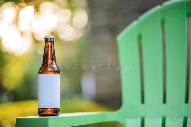Pustej etykietki Piwna butelka na Zielonym krześle ogrodowym obraz stock Pustej etykietki Piwna butelka na Zielonym krześle ogrodowym obraz stock