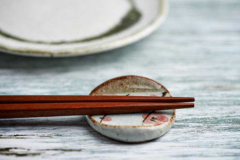 Pusty ceramika talerz, drewniani chopsticks i chopstick, odpoczywamy na nieociosanym drewnianym tle obraz stock Pusty ceramika talerz, drewniani chopsticks i chopstick, odpoczywamy na nieociosanym drewnianym tle obraz stock