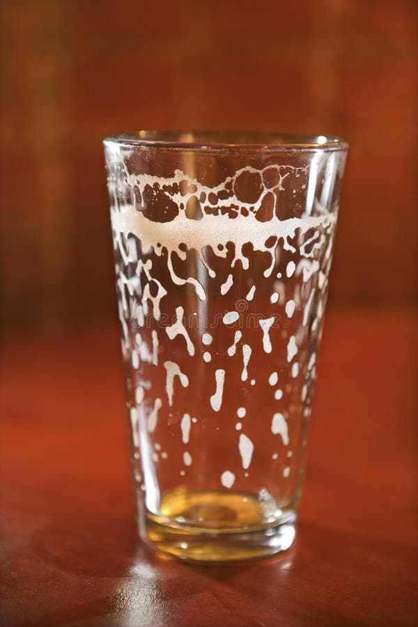 Empty beer glass on bar counter with residual foam lining the glass. Vertical shot. Empty beer glass on bar counter with residual foam lining the glass. Vertical shot.