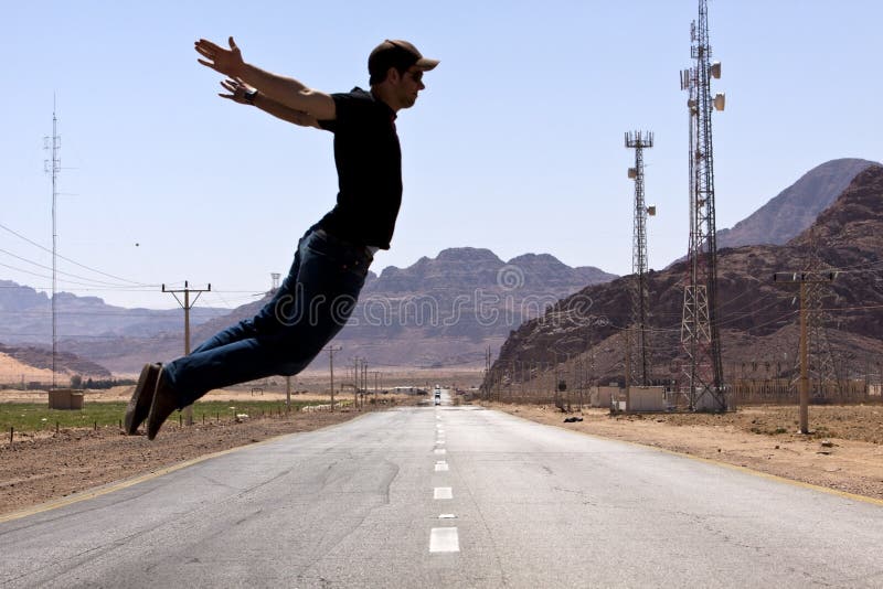 A guy performs a jumping scene above a ordinary single road which leads to some mountains near the desert Wadi Rum of jordan. A guy performs a jumping scene above a ordinary single road which leads to some mountains near the desert Wadi Rum of jordan.