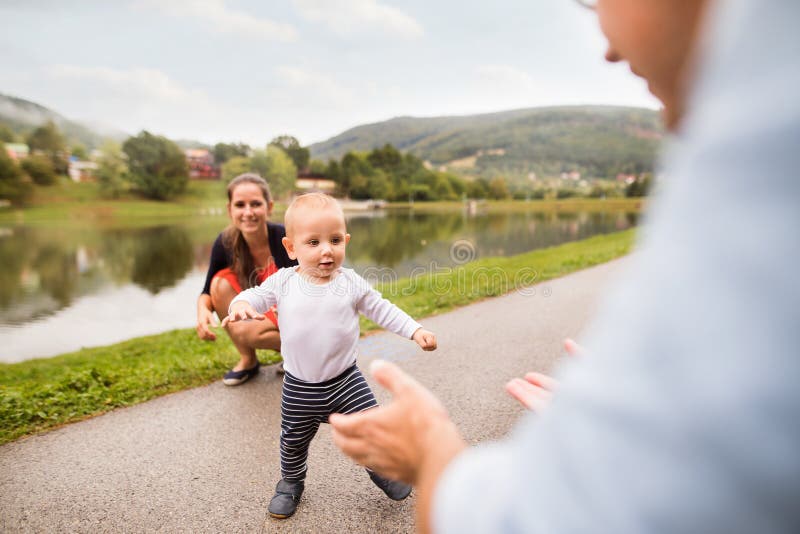 Pys med föräldrar som gör första steg. Gulliga pysdanandeförsta steg i natur Ung familjspendindtid i natur unga vuxen människa