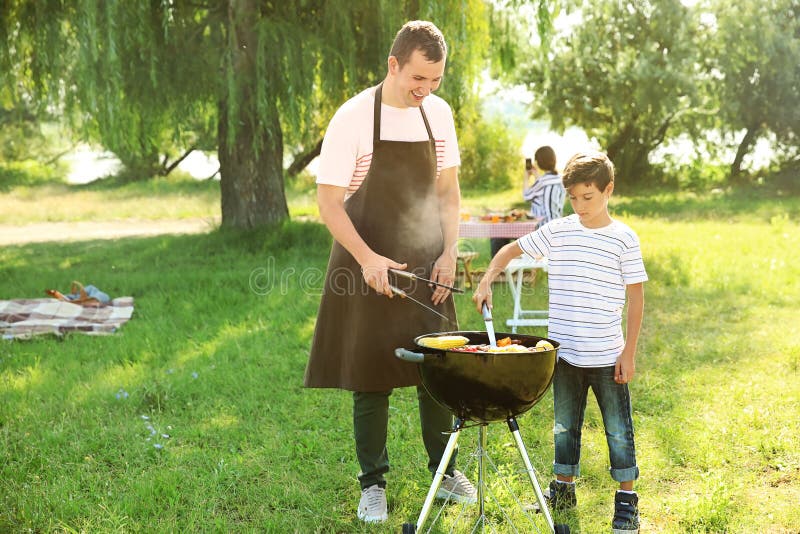 Pys med hans fader som utomhus lagar mat smaklig mat på grillfestgaller royaltyfri fotografi Pys med hans fader som utomhus lagar mat smaklig mat på grillfestgaller royaltyfri fotografi