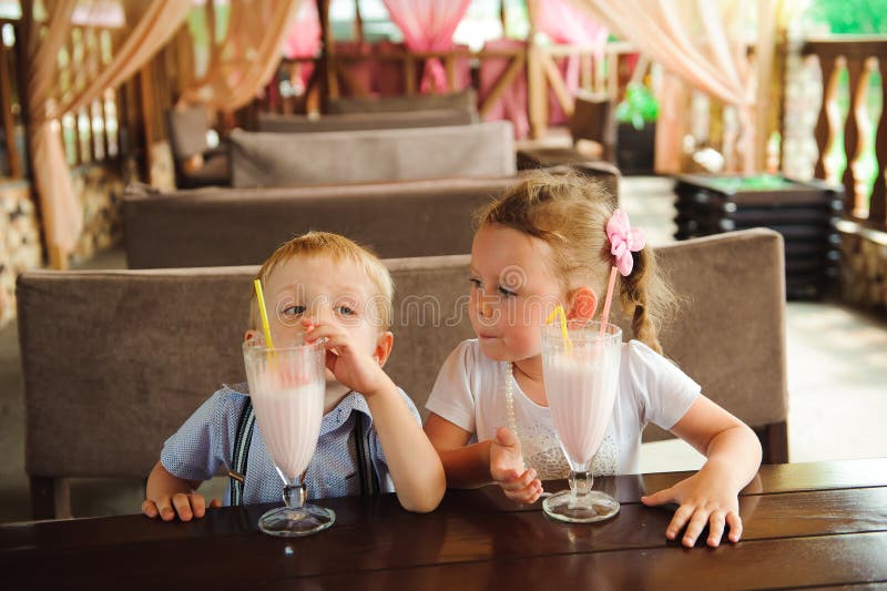 Pys och flicka som utomhus dricker milkshakar i ett kafé royaltyfria bilder