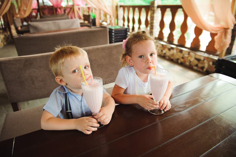 Pys och flicka som utomhus dricker milkshakar i ett kafé royaltyfria bilder