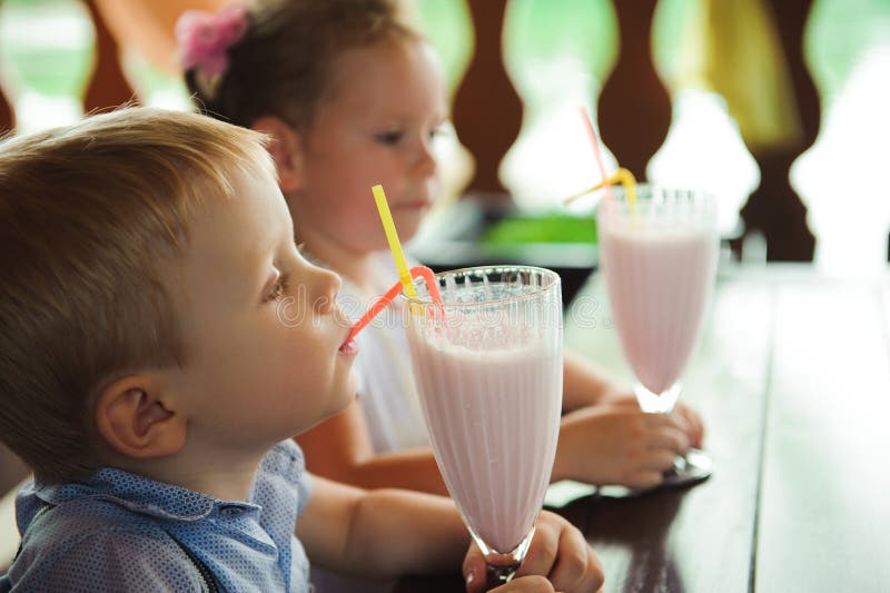 Pys och flicka som utomhus dricker milkshakar i ett kafé royaltyfria bilder