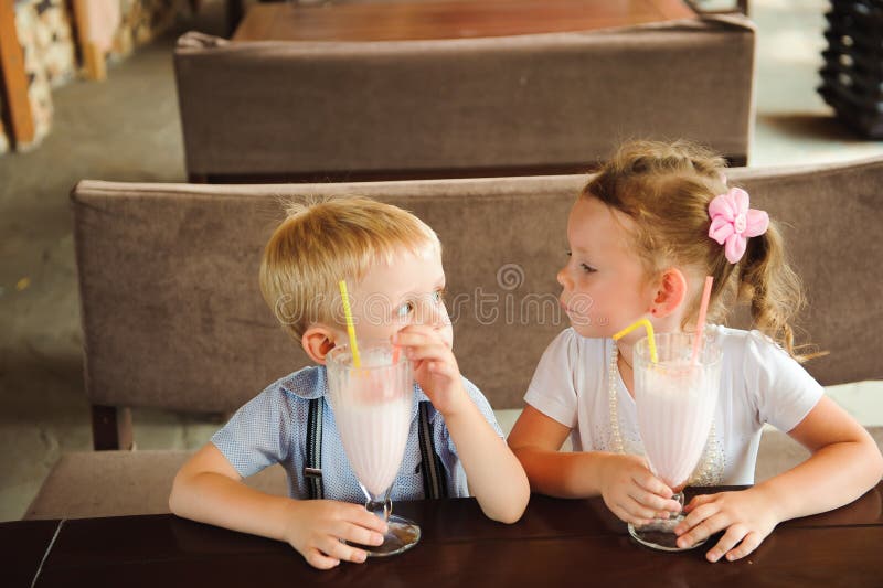 Pys och flicka som utomhus dricker milkshakar i ett kafé royaltyfri bild