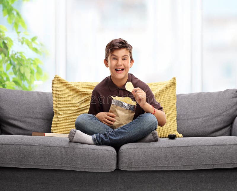 Joyful little boy sitting on a sofa and eating potato chips. Joyful little boy sitting on a sofa and eating potato chips