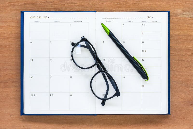Página abierta del calendario de julio del libro del planificador del diario con los vidrios y pluma en el th foto de archivo libre de regalías Página abierta del calendario de julio del libro del planificador del diario con los vidrios y pluma en el th foto de archivo libre de regalías