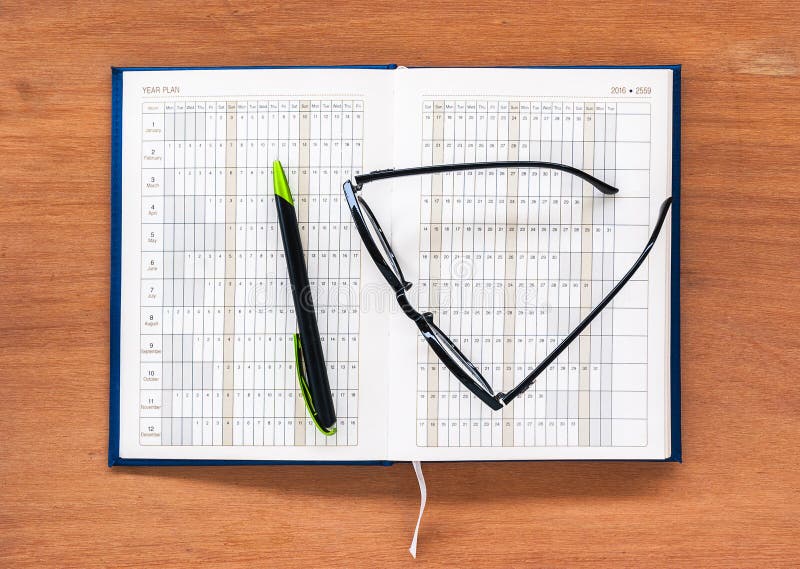 Página abierta del calendario del libro del planificador del diario con los vidrios y la pluma fotografía de archivo Página abierta del calendario del libro del planificador del diario con los vidrios y la pluma fotografía de archivo