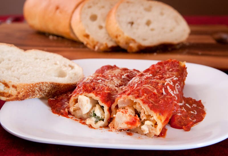Two tasty stuffed manicotti shells topped with pasta sauce and Italian bread on the side. Two tasty stuffed manicotti shells topped with pasta sauce and Italian bread on the side