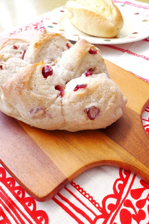 A photograph showing two delicious freshly baked bread loafs, a walnut and cranberry loaf on the left, and a butter garlic bread on the right. Hot baked golden brown loafs for breakfast theme. Taken with wooden oar shaped board for serving and cutting, against pretty table cloth of red and white floral background. A photograph showing two delicious freshly baked bread loafs, a walnut and cranberry loaf on the left, and a butter garlic bread on the right. Hot baked golden brown loafs for breakfast theme. Taken with wooden oar shaped board for serving and cutting, against pretty table cloth of red and white floral background.