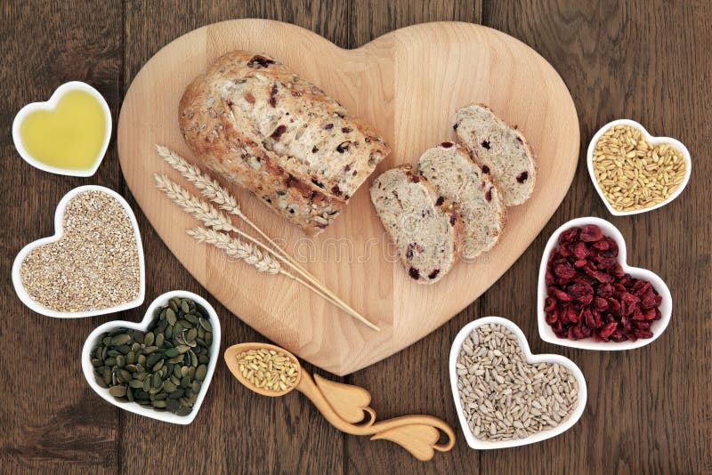 Cranberry and seed bread loaf on a heart shaped wooden board with wheat sheaths, lovespoon with grain, pumpkin and sunflower seeds, cranberries, oatmeal and olive oil on old oak background. Cranberry and seed bread loaf on a heart shaped wooden board with wheat sheaths, lovespoon with grain, pumpkin and sunflower seeds, cranberries, oatmeal and olive oil on old oak background.