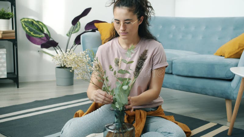 Påtlig assisk hemmafru som arrangerar blommor i vacker vase på golvet hemma stock video