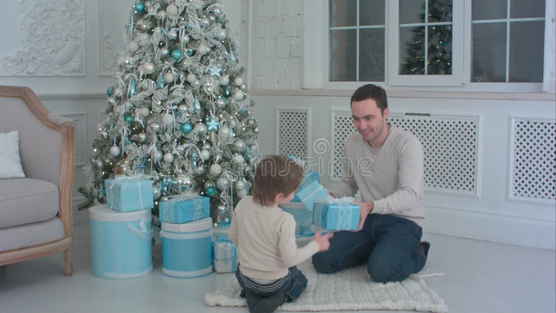 Père de sourire et ses cadeaux de Noël d'ouverture de fils dans le salon photo stock Père de sourire et ses cadeaux de Noël d'ouverture de fils dans le salon photo stock