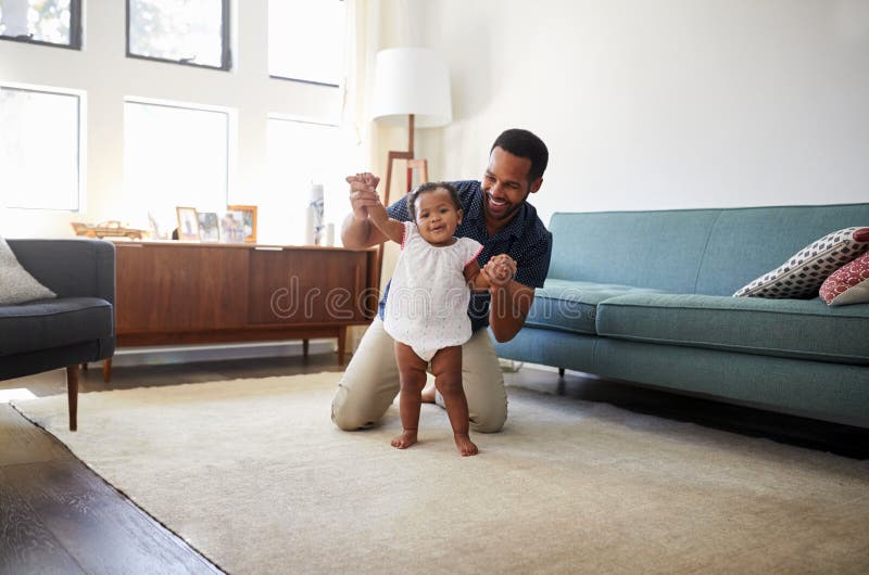 Père Encouraging Baby Daughter pour prendre des premières étapes à la maison photo libre de droits Père Encouraging Baby Daughter pour prendre des premières étapes à la maison photo libre de droits
