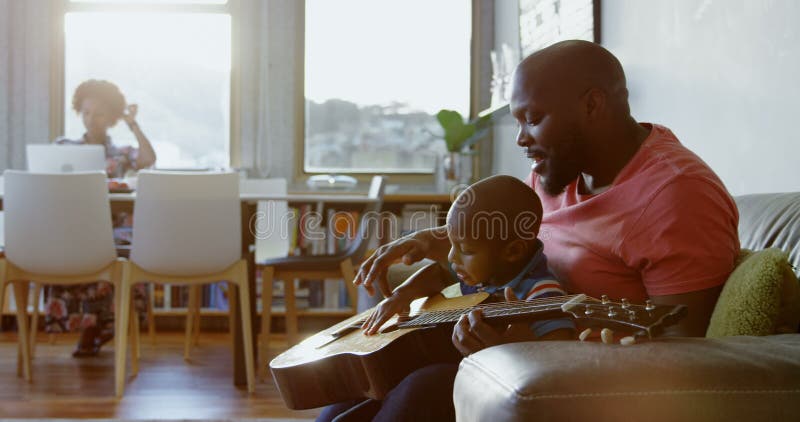 Père enseignant à son fils comment jouer la guitare à la maison 4k banque de vidéos