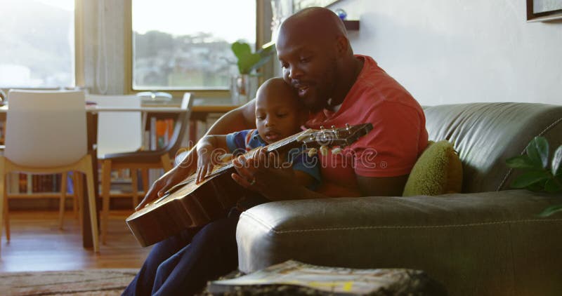Père enseignant à son fils comment jouer la guitare à la maison 4k banque de vidéos
