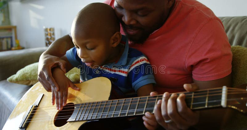 Père enseignant à son fils comment jouer la guitare à la maison 4k banque de vidéos