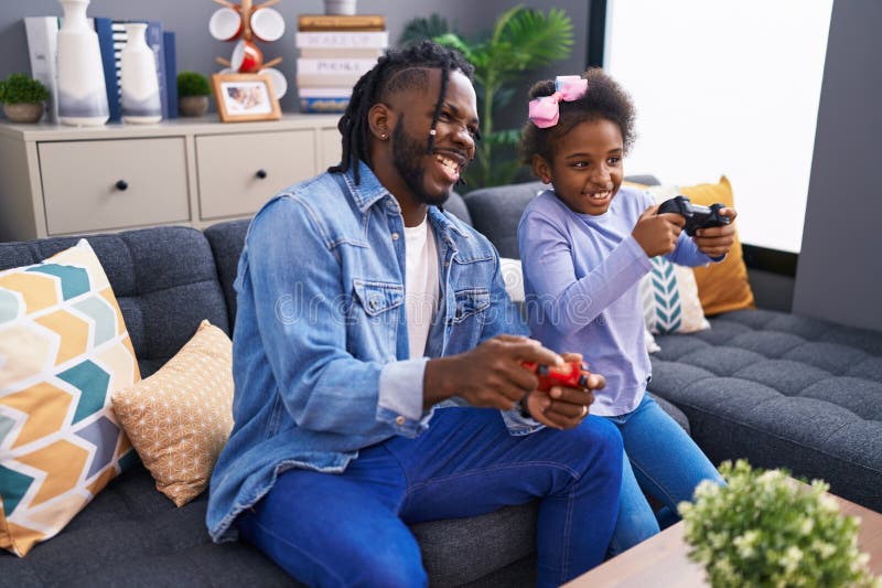 Père et fille jouant à un jeu vidéo assis sur le canapé à la maison photographie stock