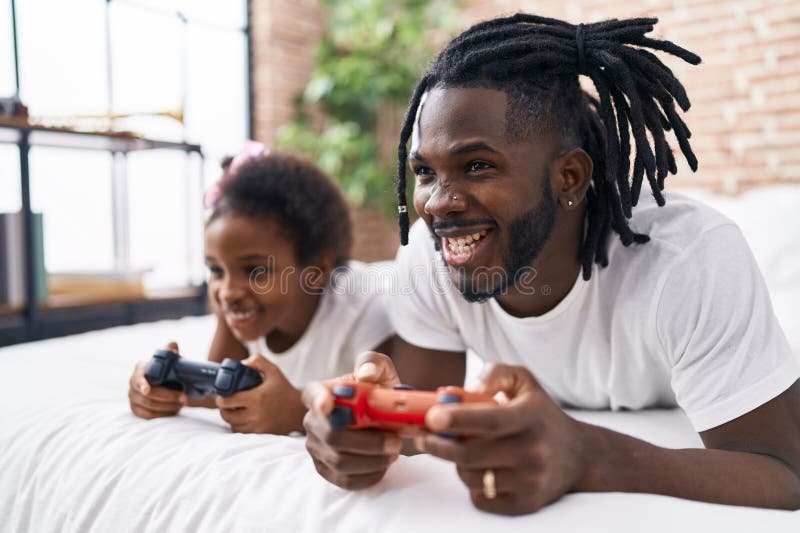 Père et fille jouant à un jeu vidéo couché sur le lit dans la chambre image stock