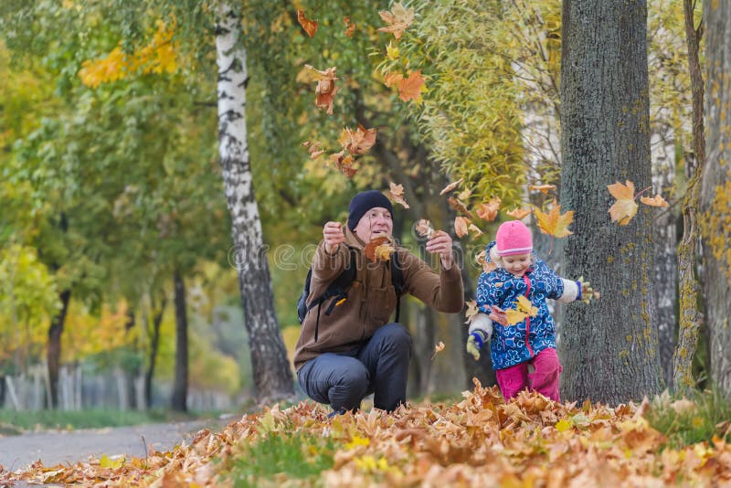 Père heureux avec la petite fille jetant en l'air vers le haut des feuilles d'automne jaunes en parc dehors photo stock