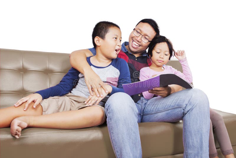 Père lisant un livre à ses enfants sur le divan images stock