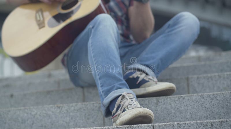 Pé de um ritmo guitarrista irreconhecível batendo nas escadas urbanas Músico caucasiano masculino tocando violão ao ar livre