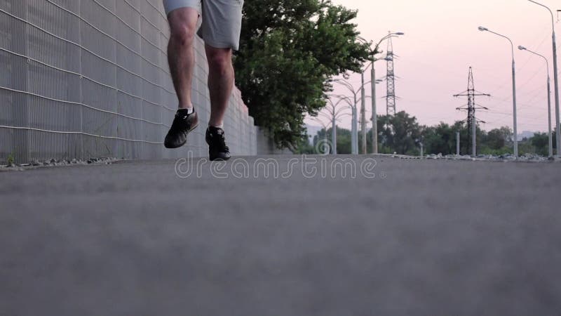 Pés de um corredor que corre no parque no asfalto no crepúsculo Movimento lento