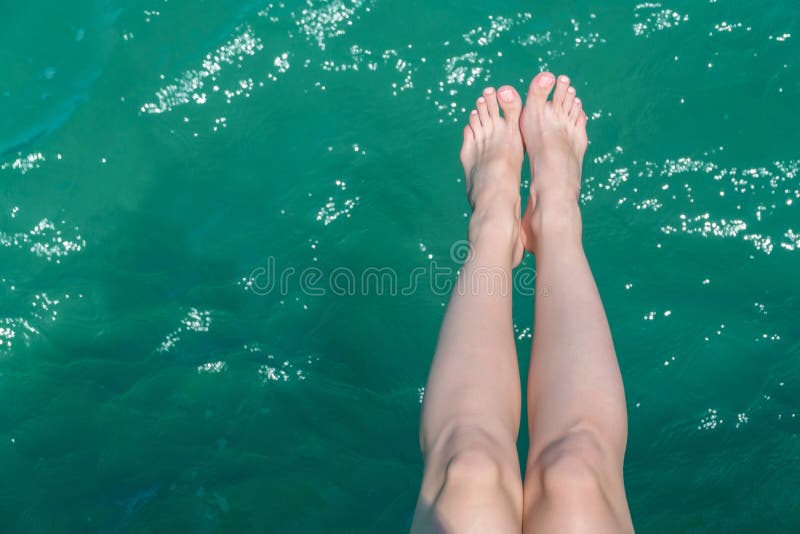Pés fêmeas novos que penduram sobre a água do mar foto de stock Pés fêmeas novos que penduram sobre a água do mar foto de stock