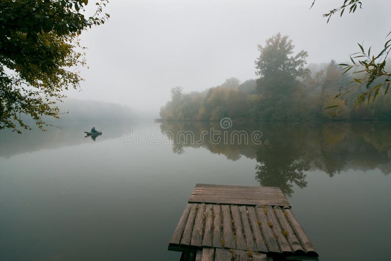 Pêcheur dans un canot en caoutchouc pêchant avec des tiges sur un petit lac, toujours surface de l'eau image stock Pêcheur dans un canot en caoutchouc pêchant avec des tiges sur un petit lac, toujours surface de l'eau image stock