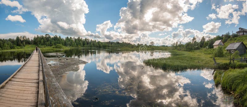 Północna Rosyjska wioska Isady Letni dzień, Emca rzeka, stare chałupy na brzeg, stary drewniany most i chmur odbicia