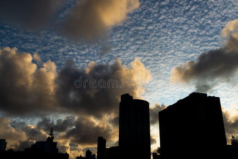 Pôr do sol dramático e bonito com nuvens coloridas e parte de edifícios residenciais na silhueta imagem de stock
