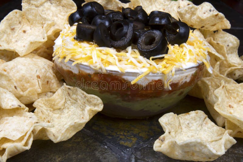 Layered bean dip in glass bowl topped with black olives and surrounded with corn chips. Layered bean dip in glass bowl topped with black olives and surrounded with corn chips