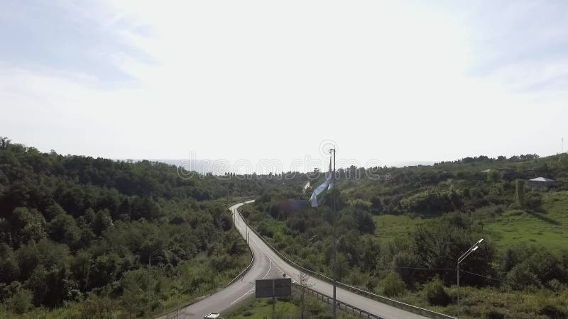 Quadcopter muestra la bandera que agita de Abjasia en el fondo del camino el día soleado