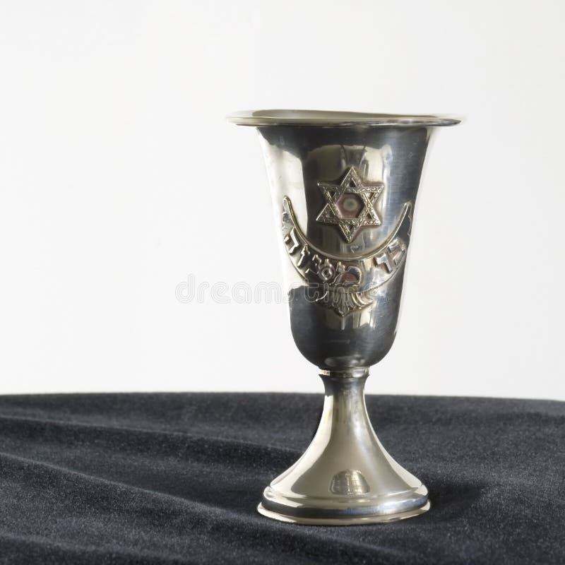 Old antique sterling silver Kiddish cup for Jewish Sabbath or jewish holidays sitting on black velvet in front of white background front of cup says Bar Mitzvah in hebrew letters and having the jewish star the star of david above the hebrew words and kiddish cups like this one are typically given to jewish boys when they have their bar mitzvah at age 13 and they then use them throughout their lives for ritual purposes and by jewish women. Old antique sterling silver Kiddish cup for Jewish Sabbath or jewish holidays sitting on black velvet in front of white background front of cup says Bar Mitzvah in hebrew letters and having the jewish star the star of david above the hebrew words and kiddish cups like this one are typically given to jewish boys when they have their bar mitzvah at age 13 and they then use them throughout their lives for ritual purposes and by jewish women