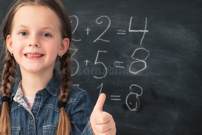 Math class. Smart smiling young girl with happy facial expression, showing thumb up over chalkboard background with sums. Math class. Smart smiling young girl with happy facial expression, showing thumb up over chalkboard background with sums.