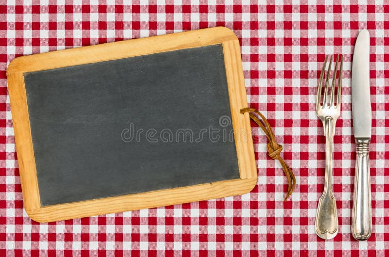 Quadro-negro vazio com pratas em uma toalha de mesa imagem de stock royalty free Quadro-negro vazio com pratas em uma toalha de mesa imagem de stock royalty free