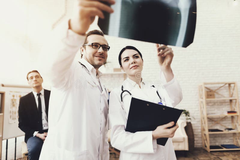 Qualified doctor with stethoscope and nurse examining x-ray of businessman at clinic. stock photo Qualified doctor with stethoscope and nurse examining x-ray of businessman at clinic. stock photo