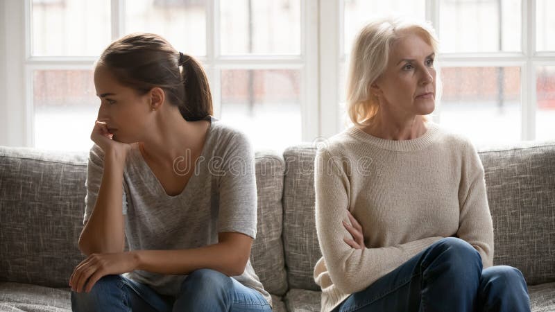 Elderly mother and grown up daughter sit on couch separately
