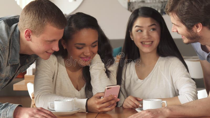 Quatre amis observent quelque chose sur le smartphone au café photographie stock libre de droits Quatre amis observent quelque chose sur le smartphone au café photographie stock libre de droits