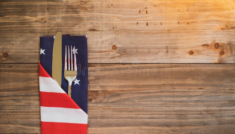 Fourth of July Table Place Setting with silverware and flag napkin on rustic wood background with room or space for copy, text, or your words.  It`s an extra wide horizontal with warm light leaks. Fourth of July Table Place Setting with silverware and flag napkin on rustic wood background with room or space for copy, text, or your words.  It`s an extra wide horizontal with warm light leaks