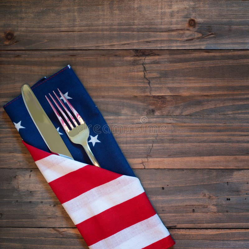 Fourth of July Table Place Setting with a fork, knife and flag napkin on rustic wood board background with room or space for copy, text, or your words.  It`s a square photo with above view. Fourth of July Table Place Setting with a fork, knife and flag napkin on rustic wood board background with room or space for copy, text, or your words.  It`s a square photo with above view