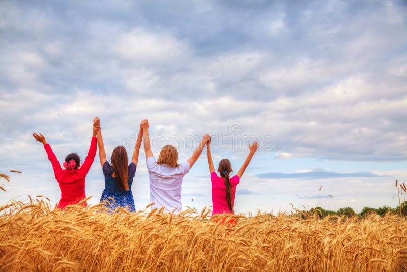 Four young people staying with raised hands at a wheat field at sunset time. Four young people staying with raised hands at a wheat field at sunset time