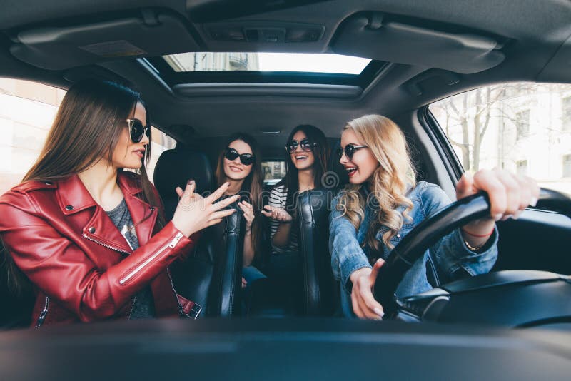 Quatro mulheres alegres novas bonitas que olham felizes e brincalhão ao sentar-se no carro fotos de stock Quatro mulheres alegres novas bonitas que olham felizes e brincalhão ao sentar-se no carro fotos de stock
