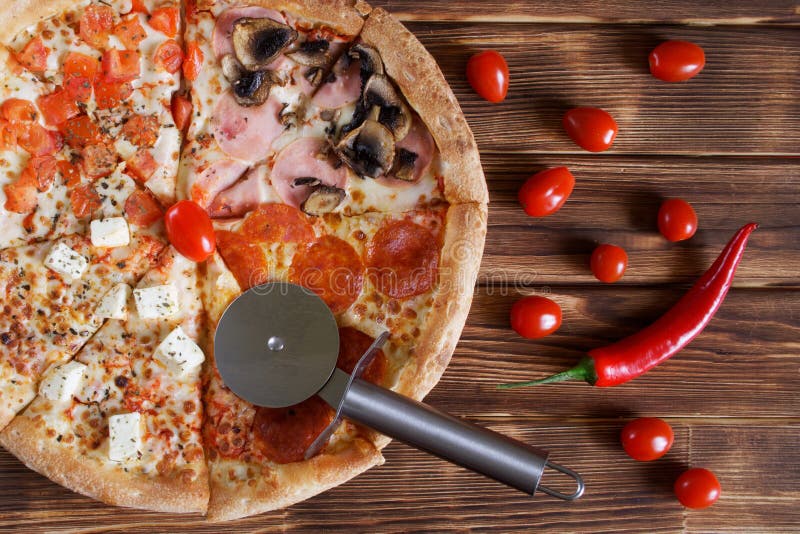 Quatro-pizza cortada com pepperoni, salame, pimentas de pimentão vermelho, cogumelos, queijo, tomates, mentiras em uma superfície imagem de stock Quatro-pizza cortada com pepperoni, salame, pimentas de pimentão vermelho, cogumelos, queijo, tomates, mentiras em uma superfície imagem de stock