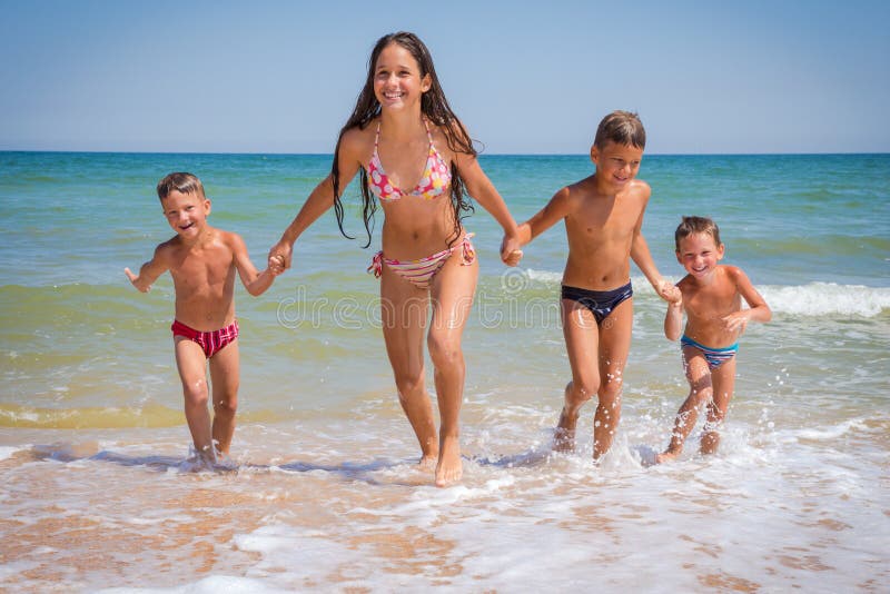 Quattro bambini che corrono dal mare sulla spiaggia immagine stock Quattro bambini che corrono dal mare sulla spiaggia immagine stock