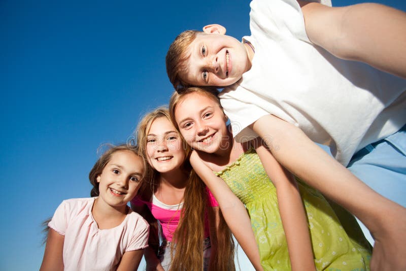 Quattro bei bambini felici che esaminano macchina fotografica dalla cima nel giorno e nel cielo blu di estate soleggiati esaminan fotografie stock libere da diritti Quattro bei bambini felici che esaminano macchina fotografica dalla cima nel giorno e nel cielo blu di estate soleggiati esaminan fotografie stock libere da diritti