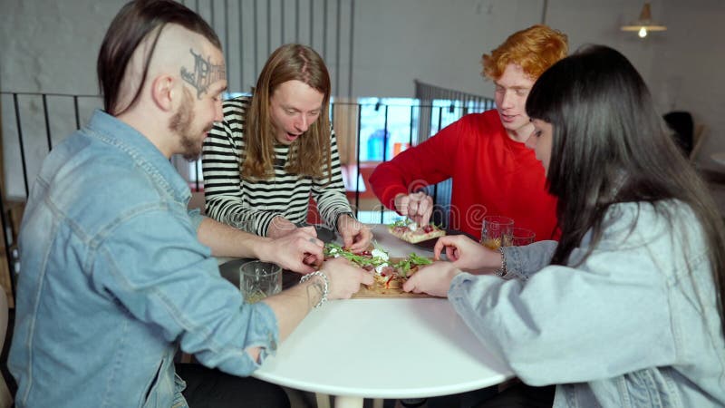 Quattro giovani caucasici uomini e donne che condividono la pizza seduti a tavola al ristorante. amici millenari rilassati