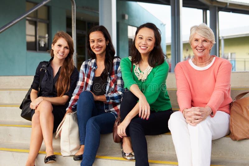 Quattro insegnanti femminili che si siedono sui punti all'entrata della scuola